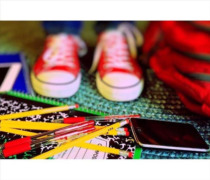 child wearing sneakers surrounded by school supplies - pens, pencils, notebook, back pack