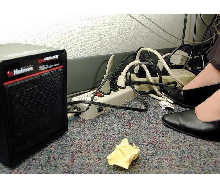 A few fire hazards are shown underneath of an office desk, including wires, a space heater, and loose paper.